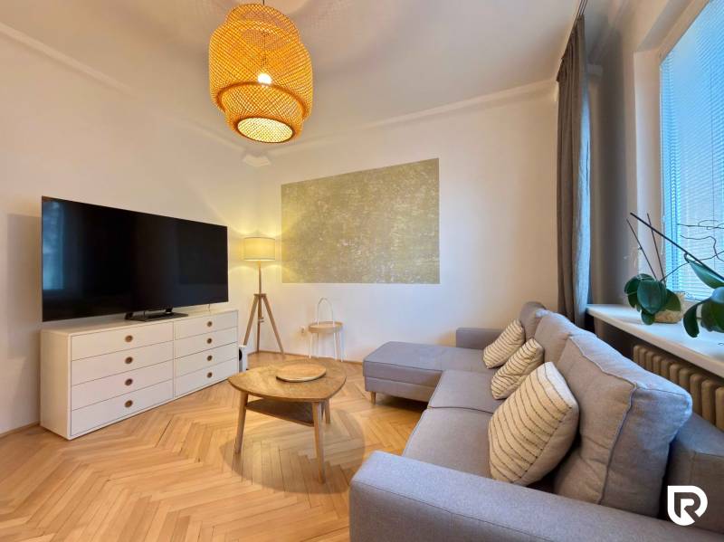 2-izbový byt 45m2 | Sklenárová - Ružinov - Obývačka v 2-izbovom byte s podlahou s dreveným dekorom, sedačkou a TV.