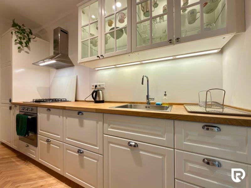 2-izbový byt 45m2 | Sklenárová - Ružinov - Svetlá kuchyňa v 2-izbovom byte s podlahou s dreveným dekorom a bielymi skrinkami.