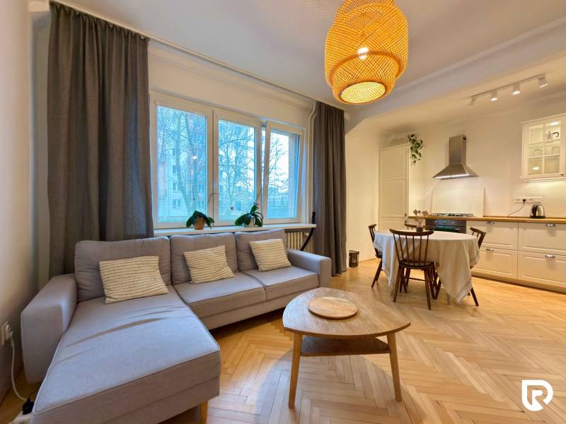 2-izbový byt 45m2 | Sklenárová - Ružinov - Obývacia izba s kuchyňou a jedálenským stolom, podlaha s dreveným dekorom, svetlá sedačka.