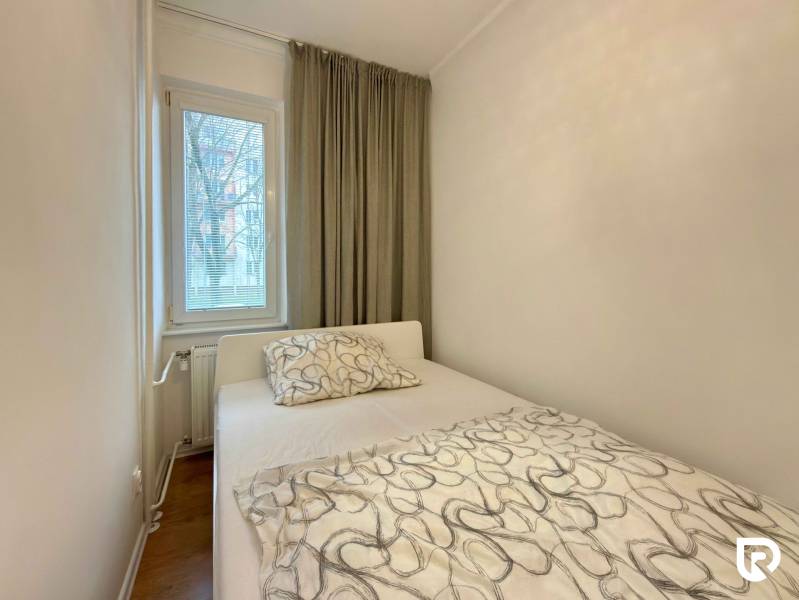 2-izbový byt 45m2 | Sklenárová - Ružinov - Spálňa v 2-izbovom byte s posteľou, oknom a závesmi, podlaha s dreveným dekorom.