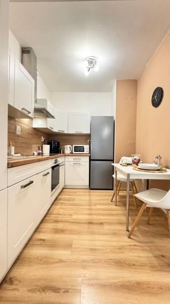 Prenájom 2 izbový byt Trenčín s vlastným parkovaním a terasou - Kuchyňa v 2-izbovom byte s bielymi skrinkami a podlahou s dreveným dekorom.