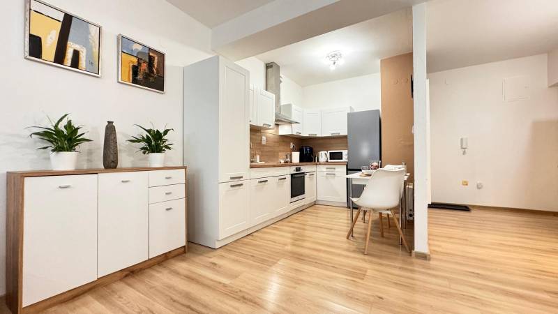 Prenájom 2 izbový byt Trenčín s vlastným parkovaním a terasou - Kuchyňa v 2-izbovom byte s bielymi skrinkami a podlahou s dreveným dekorom.