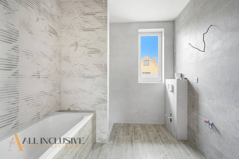 Na predaj 4-izbové novostavby, Veľká Paka - Kúpeľňa v rodinnom dome s vaňou, sivými obkladmi a podlahou s dreveným dekorom.