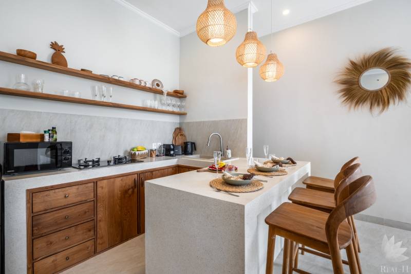 LUXUSNÁ 3-SPÁLŇOVÁ VILA S BAZÉNOM – CANGGU, BALI - Kuchyňa vily so štýlovými drevenými elementmi, barovými stoličkami a závesnými lampami.