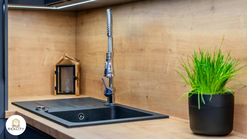 PRENÁJOM | 3i byt v centre Prešova | ZARIADENÝ - Kuchynský kút v 3-izbovom byte s čiernym drezom, dekorom dreva a rastlinou.