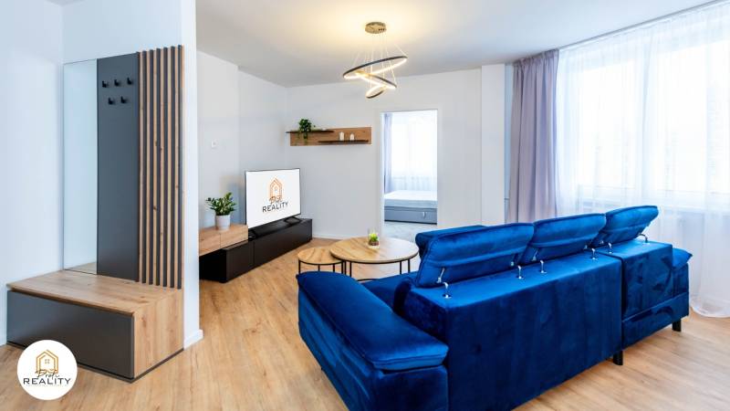 PRENÁJOM | 3i byt v centre Prešova | ZARIADENÝ - Obývačka v 3-izbovom byte s modrou pohovkou a podlahou s dreveným dekorom.