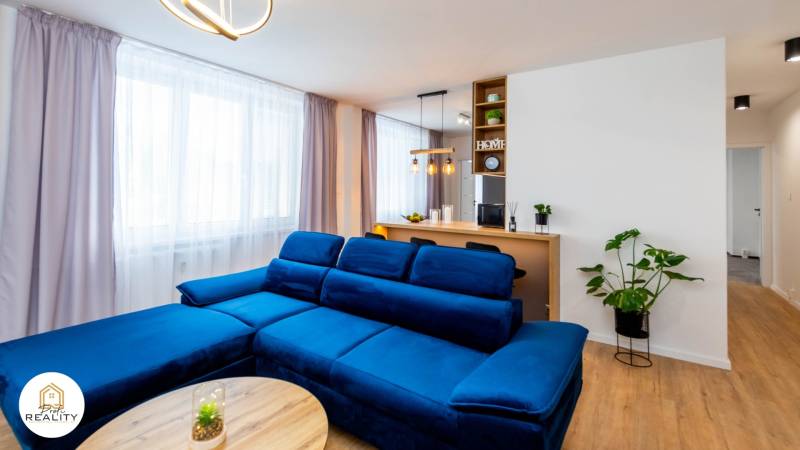 PRENÁJOM | 3i byt v centre Prešova | ZARIADENÝ - Obývačka v 3-izbovom byte s modrou sedačkou, podlaha s dreveným dekorom, interiérové rastliny.