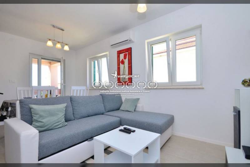 PRIVLAKA - BYT S4- dvojizbový byt 63,42 m2 vzdialený 150 m od mora - Obývačka s šedou pohovkou, konferenčný stolík a jedálenský stôl v 2-izbovom byte.