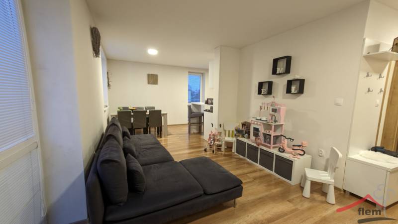 2-izbový byt na predaj, Vráble – sídl. Lúky, 56 m2 - Obývacia izba v 2-izbovom byte s podlahou s dreveným dekorom a detským kútikom.