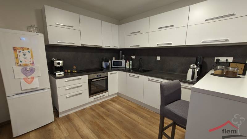 2-izbový byt na predaj, Vráble – sídl. Lúky, 56 m2 - Kuchyňa v 2-izbovom byte s podlahou s dreveným dekorom a bielymi skrinkami.