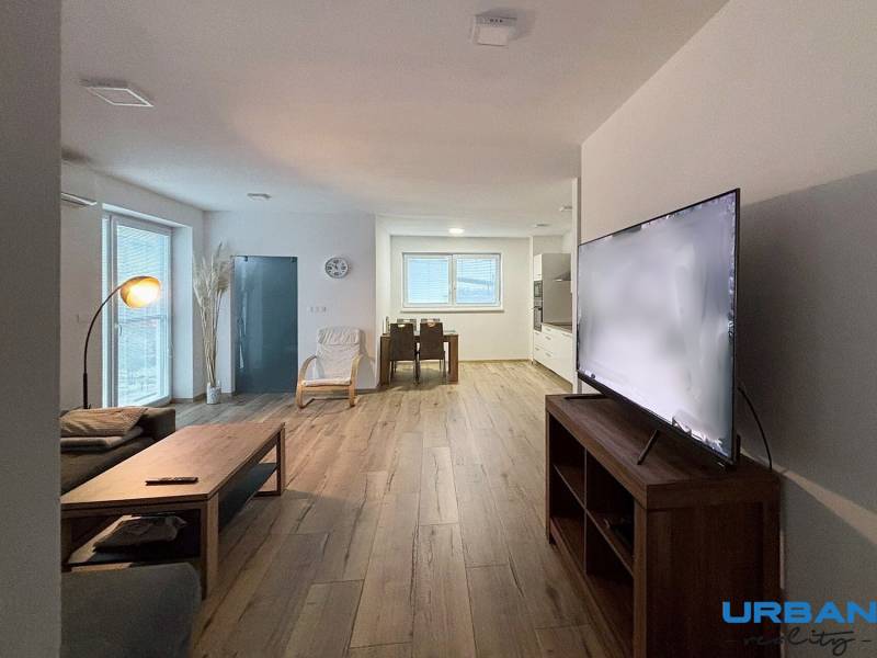 Moderný 3-izbový byt so záhradou Šamorín-Kráľovianky - Obývacia izba v 3-izbovom byte s pohovkou, televízorom a podlahou s dreveným dekorom.