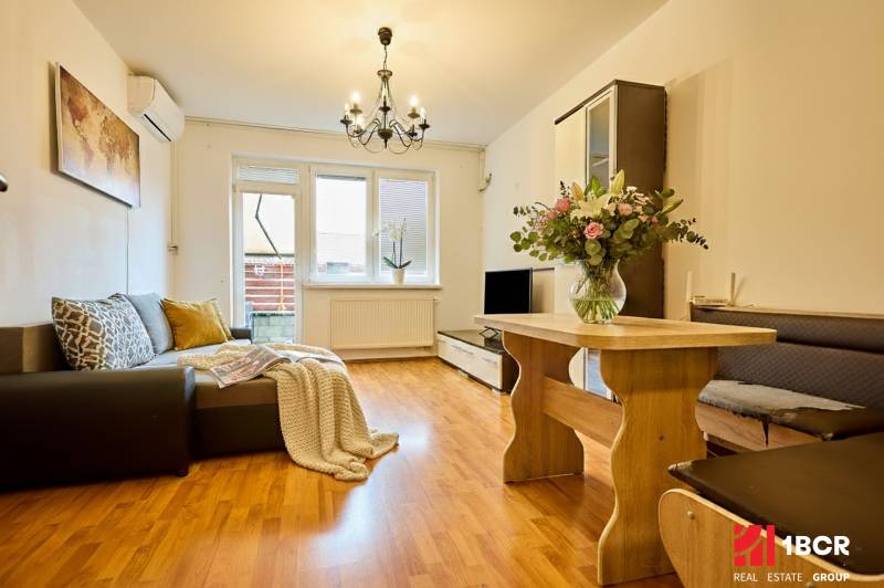 2-IZB. BYT, ČIASTOČNE ZARIADENÝ, TERASA , MOSTI PRI BRATISLAVE  - Obývacia izba v 2-izbovom byte s podlahou s dreveným dekorom a pohovkou.