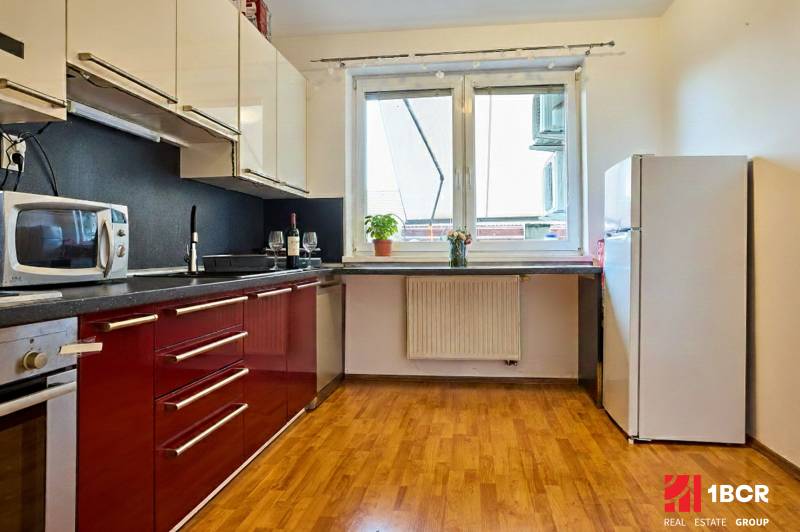 2-IZB. BYT, ČIASTOČNE ZARIADENÝ, TERASA , MOSTI PRI BRATISLAVE  - Kuchyňa v 2-izbovom byte s červenými skrinkami a podlahou s dreveným dekorom.