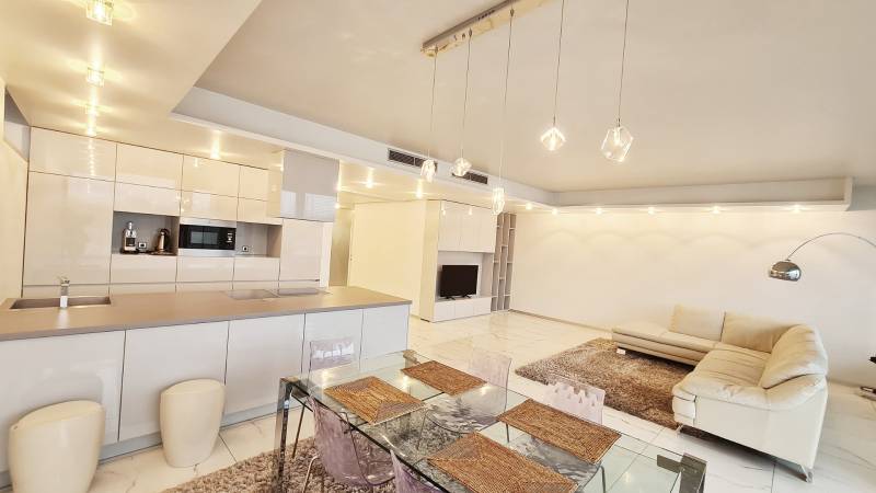 Luxusný 3-izb. byt s famóznym výhľadom na Dunaj, River Park - Priestranný obývací priestor v 3-izbovom byte s kuchyňou, jedálenským stolom a pohodlnou sedačkou.