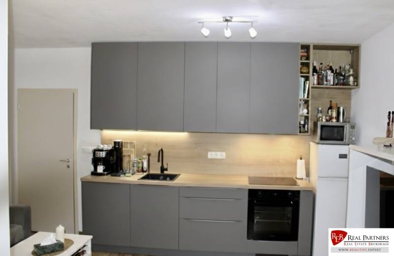 Prenájom 2-izb bytu Dlhé diely - Kuchyňa v 2-izbovom byte s tmavosivou linkou a spotrebičmi.