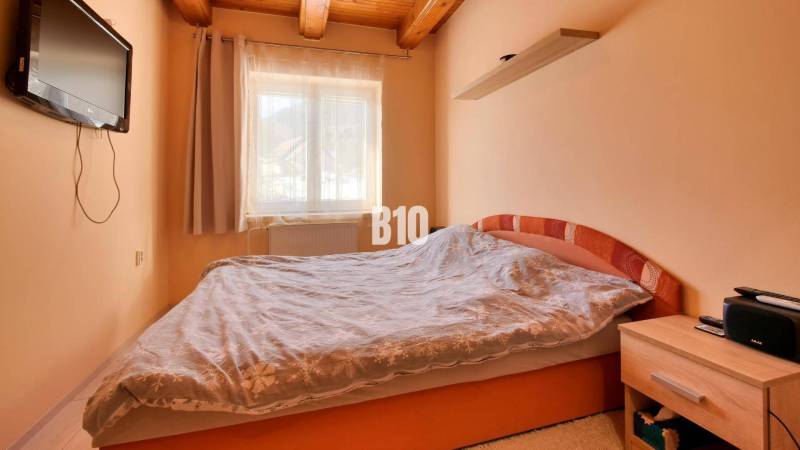 Praktický 8-izbový rodinný dom na Bystričke: Vhodný pre veľkú rodinu z - Spálňa v rodinnom dome s televízorom, posteľou a drevenými stropnými trámami.