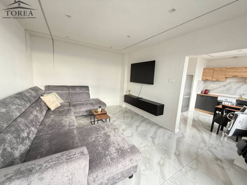 Prenájom kompletne zrekonštruovaný 2izbový byt Topoľčany s balkónom - Obývacia izba s šedou sedacou súpravou, televízorom na stene a otvorenou kuchyňou v 2-izbovom byte.