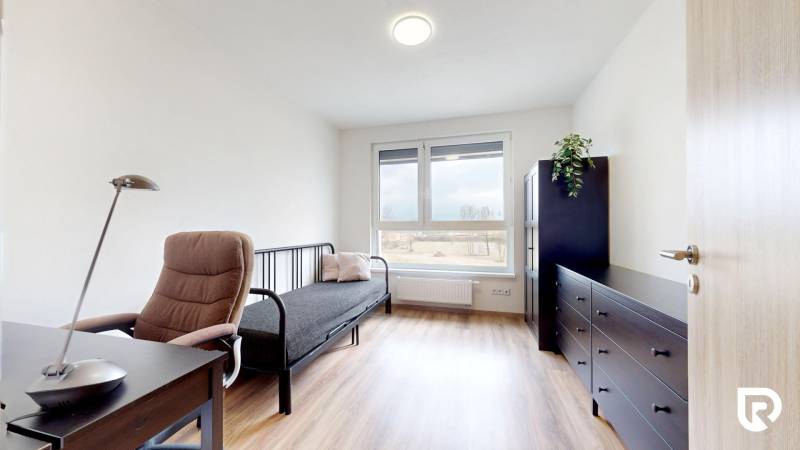 | 3-izbový byt v novostavbe, ul. Odevná + parking | Trenčín  - Izba s podlahou s dreveným dekorom, pracovným stolom a pohovkou v 3-izbovom byte.