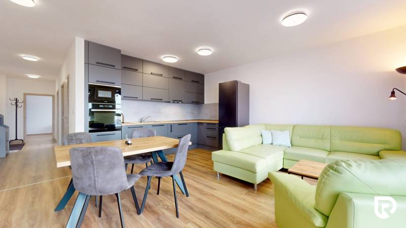 | 3-izbový byt v novostavbe, ul. Odevná + parking | Trenčín  - Kuchyňa s obývačkou v 3-izbovom byte, zelená sedačka, podlaha s dreveným dekorom.