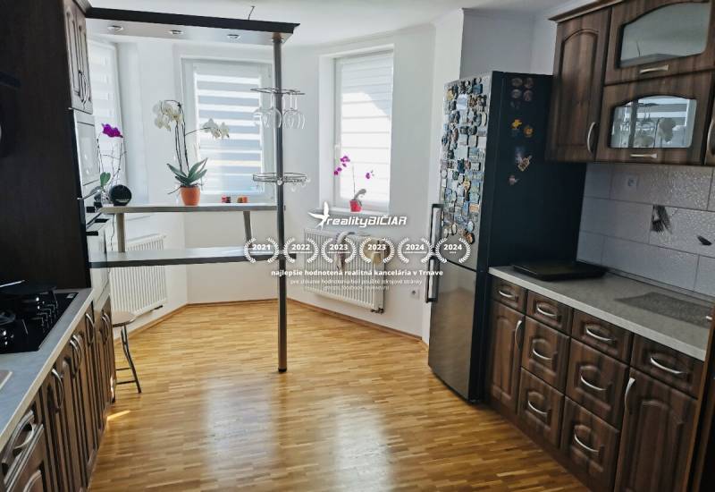 Moderný rodinný dom v Ratkovciach s priestrannou pivnicou - Kuchyňa v rodinnom dome s podlahou s dreveným dekorom, tmavým nábytkom a barovým pultom.