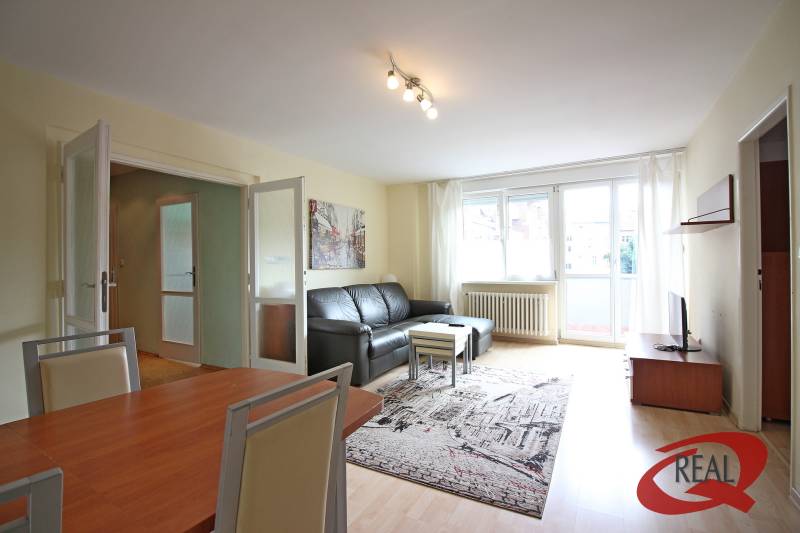 **BEZ PROVÍZIE**3-IZBOVÝ BYT S BALKÓNOM A LOGGIOU NA PALISÁDACH**      - Obývačka v 3-izbovom byte s podlahou s dreveným dekorom a čiernou pohovkou.