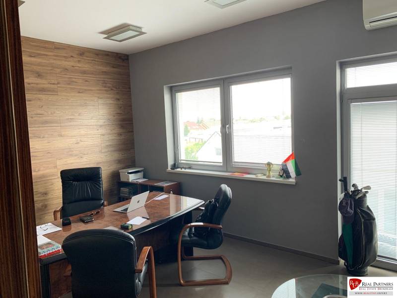 Predaj modernej administratívnej budovy v Bratislave, okres II - Kancelária s drevenými stenami, písacím stolom, čiernymi kreslami a veľkými oknami v budove.