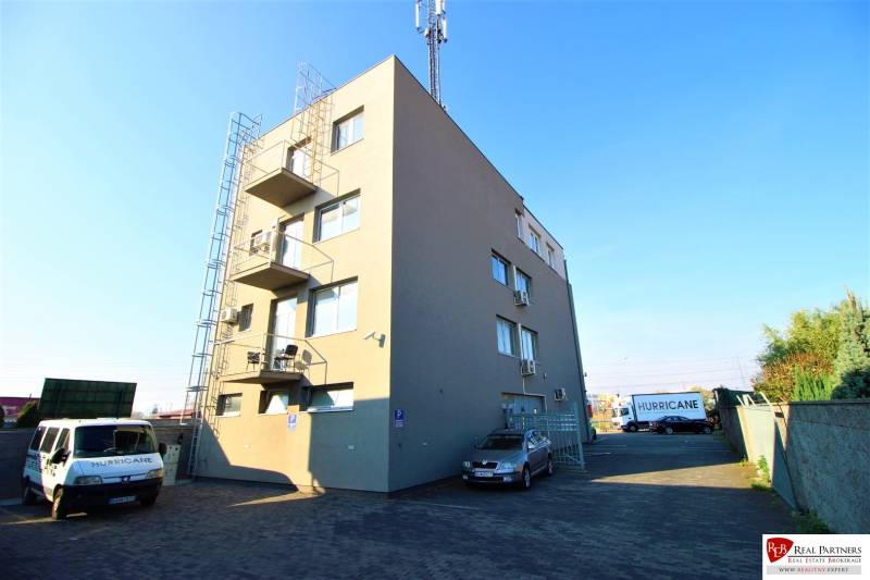 Predaj modernej administratívnej budovy v Bratislave, okres II - Budova na snímke s parkoviskom a zaparkovanými autami na pozemku.