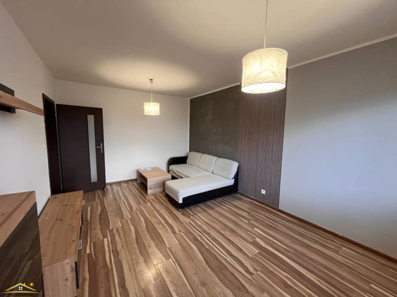 Prenájom: 2 izbový byt Žilina - Vlčince - Obývacia izba 2-izbového bytu s podlahou s dreveným dekorom, pohovkou a svietidlom.