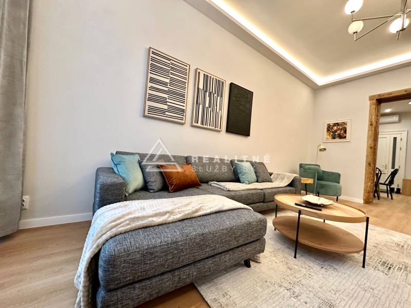 Prenájom priestranného 2-izbového bytu v absolútnom centre Košíc - Obývacia izba s pohovkou, podlahou s dreveným dekorom a umeleckými dielami v 2-izbovom byte.