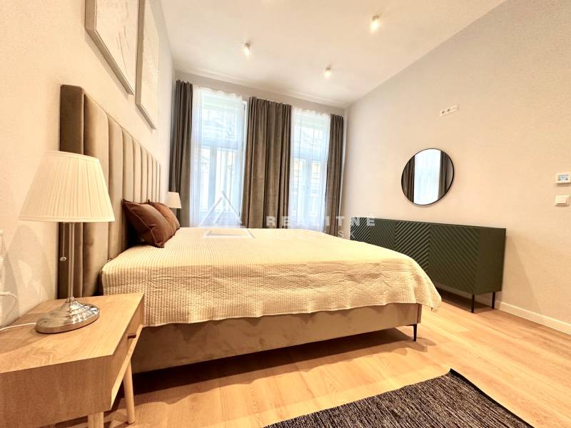 Prenájom priestranného 2-izbového bytu v absolútnom centre Košíc - Spálňa v 2-izbovom byte s veľkou posteľou, lampou a podlahou s dreveným dekorom.