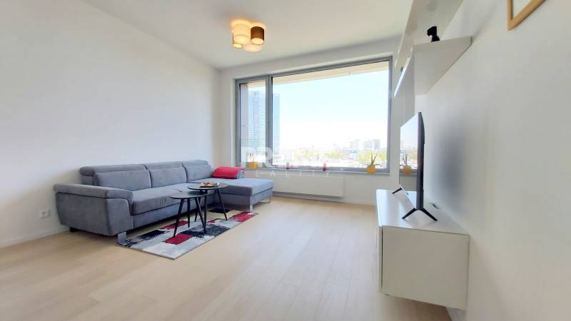 JEDINEČNÝ 2i byt, NOVOSTAVBA, KLÍMA, VÝHĽAD, PARKING, SKY PARK - Obývacia izba v 2-izbovom byte s pohovkou, televízorom a výhľadom z veľkého okna.