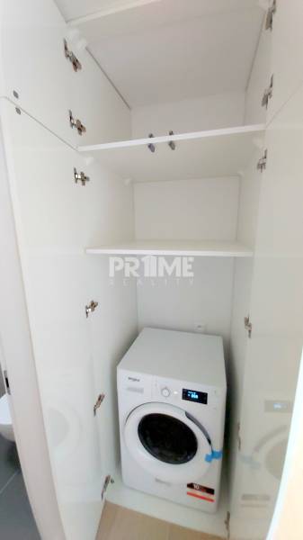 JEDINEČNÝ 2i byt, NOVOSTAVBA, KLÍMA, VÝHĽAD, PARKING, SKY PARK - Práčka zabudovaná v bielom skrini v 2-izbovom byte, úložné police nad ňou.