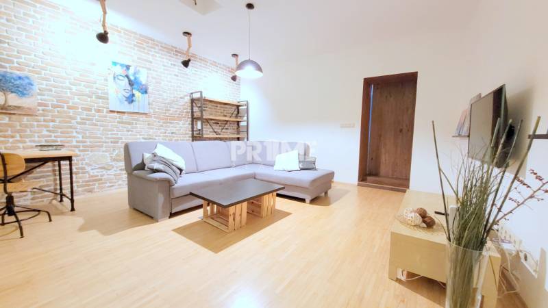 JEDINEČNÝ 2i byt, REKONŠT., 2 X .SAMOST.IZBA, Hviezdoslavovo nám.  - Obývacia izba na ulici Hviezdoslavovo námestie, 2-izbový byt s tehlovou stenou a šedou sedačkou.