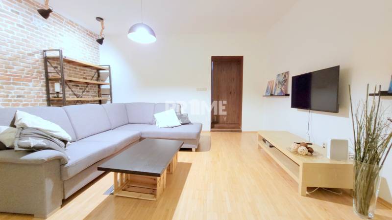 JEDINEČNÝ 2i byt, REKONŠT., 2 X .SAMOST.IZBA, Hviezdoslavovo nám.  - Priestranná obývačka s tehlovou stenou, sedačkou a televízorom na Hviezdoslavovo námestie v 2-izbovom byte.