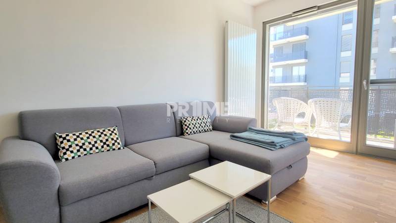 MODERNÝ 3i byt, CUBICON GARDENS, BALKÓN, PARKING, Rudolfa Mocka - Obývacia izba v 3-izbovom byte s pohovkou a balkónom, podlaha s dreveným dekorom.