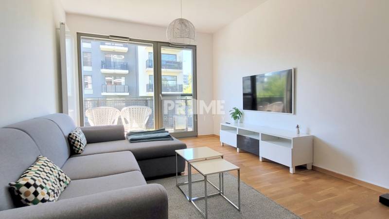 MODERNÝ 3i byt, CUBICON GARDENS, BALKÓN, PARKING, Rudolfa Mocka - Obývačka v 3-izbovom byte s podlahou s dreveným dekorom, televízorom a sivou sedačkou.