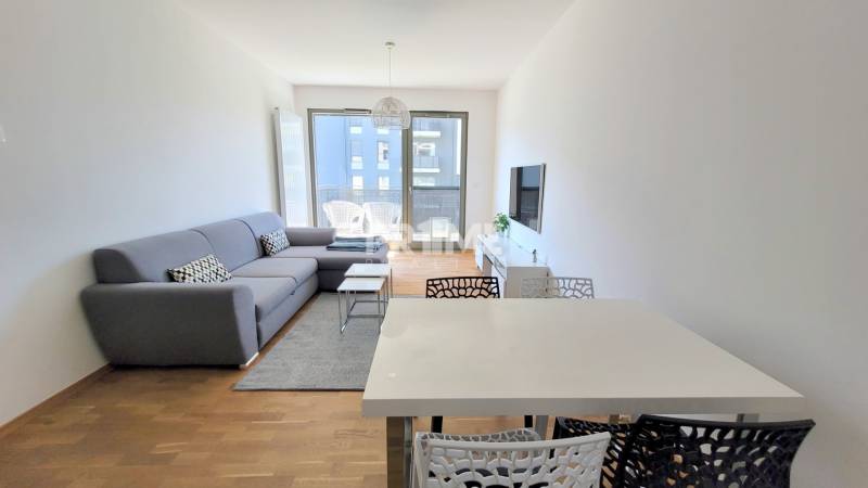 MODERNÝ 3i byt, CUBICON GARDENS, BALKÓN, PARKING, Rudolfa Mocka - Obývačka v 3-izbovom byte s pohodlnou sedačkou a podlahou s dreveným dekorom.