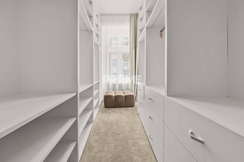  EXKLUZÍVNY, VEĽKOMETRÁŽNY 3i byt ( 130 m2 ), REKONŠTRUKCIA, CENTRUM - Úzka šatníková miestnosť s bielymi policami a béžovým kreslom v 3-izbovom byte.