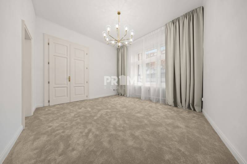  EXKLUZÍVNY, VEĽKOMETRÁŽNY 3i byt ( 130 m2 ), REKONŠTRUKCIA, CENTRUM - Priestranná miestnosť s kobercovou podlahou a veľkým oknom v 3-izbovom byte.