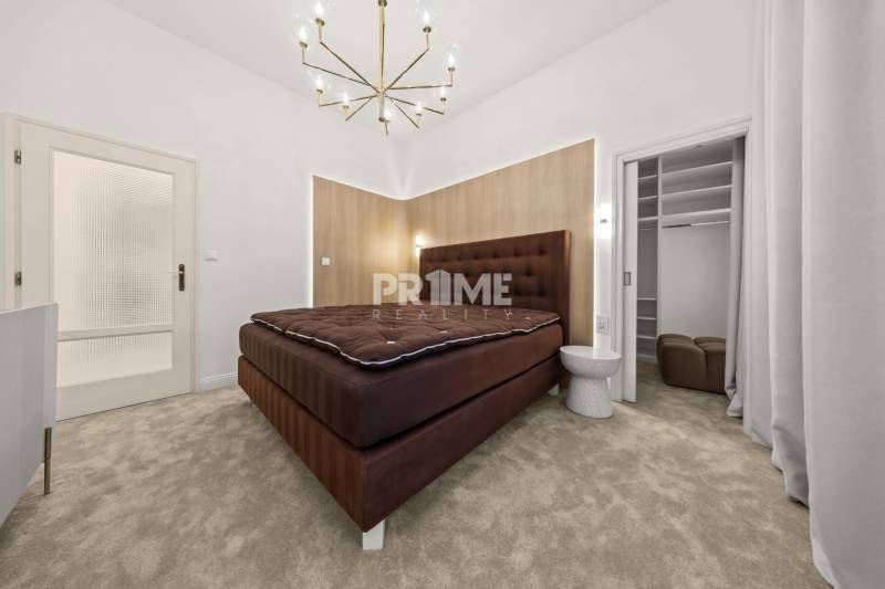  EXKLUZÍVNY, VEĽKOMETRÁŽNY 3i byt ( 130 m2 ), REKONŠTRUKCIA, CENTRUM - Spálňa so svetlým kobercom, čalúnenou posteľou a vstupom do šatníka v 3-izbovom byte.