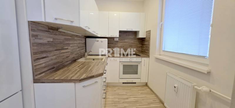 MODERNÝ 2i byt, REKONŠTRUKCIA, KLÍMA, MOZARTOVA ulica, Horský park - Kuchyňa v 2-izbovom byte, biele skrinky, podlaha s dreveným dekorom, žalúzie na oknách.