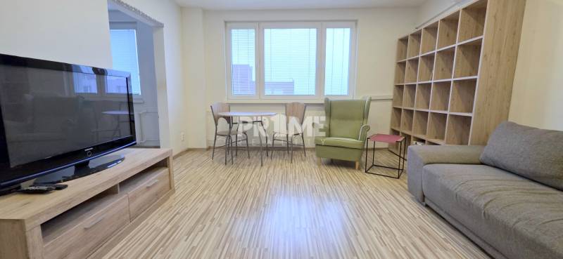 MODERNÝ 2i byt, REKONŠTRUKCIA, KLÍMA, MOZARTOVA ulica, Horský park - Obývacia izba v 2-izbovom byte s podlahou s dreveným dekorom, televíziou a policovou stenou.