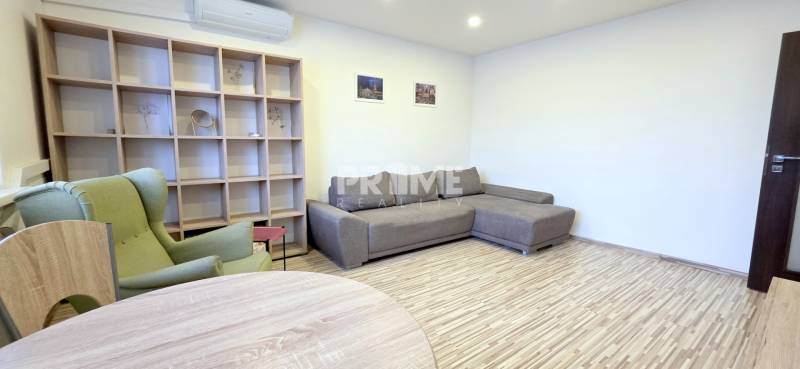 MODERNÝ 2i byt, REKONŠTRUKCIA, KLÍMA, MOZARTOVA ulica, Horský park - Obývačka v 2-izbovom byte s gaučom, kreslom a policovou stenou, podlaha s dreveným dekorom.