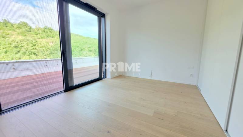 LUXUSNÝ 3i byt,PARKING,CHLADENIE,TERASA,Grand Koliba, Frankovská ulica - Izba v 3-izbovom byte s drevenou podlahou a výhľadom na zelený exteriér.