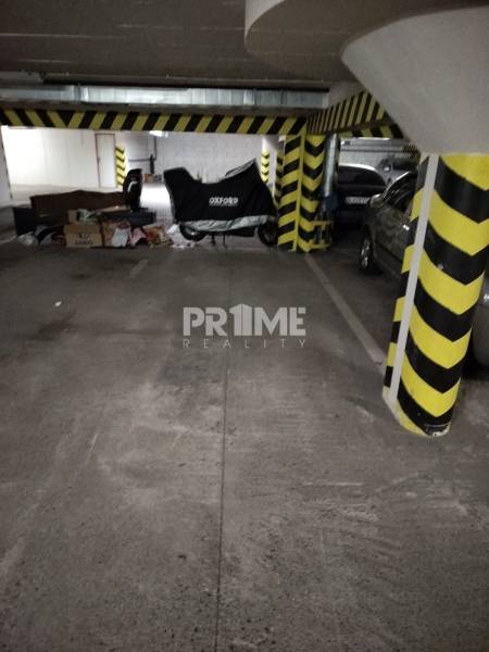 Garážové parkovacie miesto, NOVOSTAVBA, Krajná ulica, Trnávka - Parkovacie miesto v garáži s betónovou podlahou a vozidlom pod plachtou.