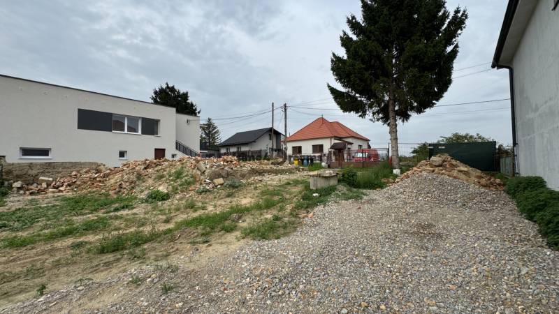 NA PREDAJ Pozemok Zbehy - Andač - Pozemky - bývanie v Andači s pohľadom na domy a kopy stavebného materiálu.