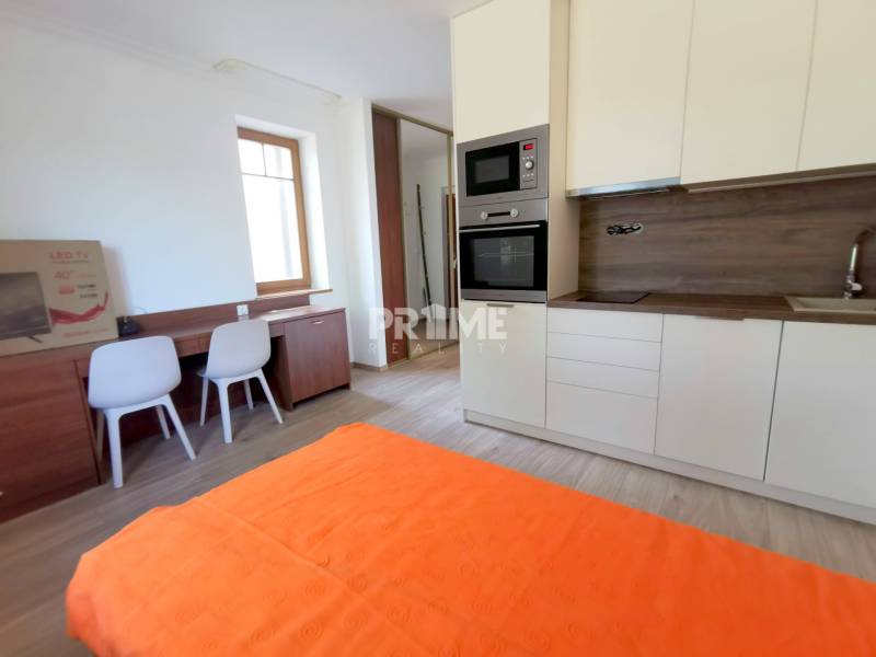 PEKNÁ GARSÓNKA, NOVOSTAVBA, KLÍMA, DRAŽDIAK HAUS, Antolská ulica - Garsónka s kuchyňou, stôl so stoličkami, posteľ a podlaha s dreveným dekorom.