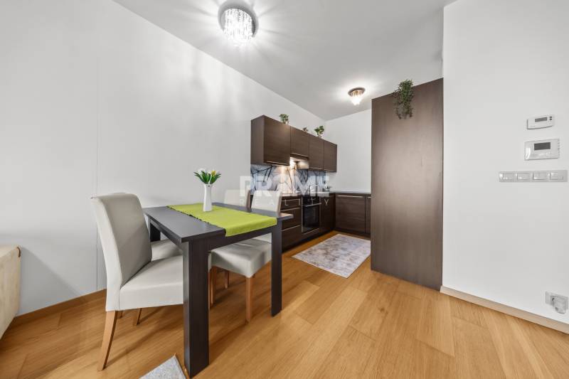 KRÁSNY 2i byt, KLÍMA, LOGGIA,VÝHĽAD,PANORAMA CITY, Landererova ulica - Jedálenský stôl a kuchyňa s tmavým nábytkom, podlaha s dreveným dekorom v 2-izbovom byte.