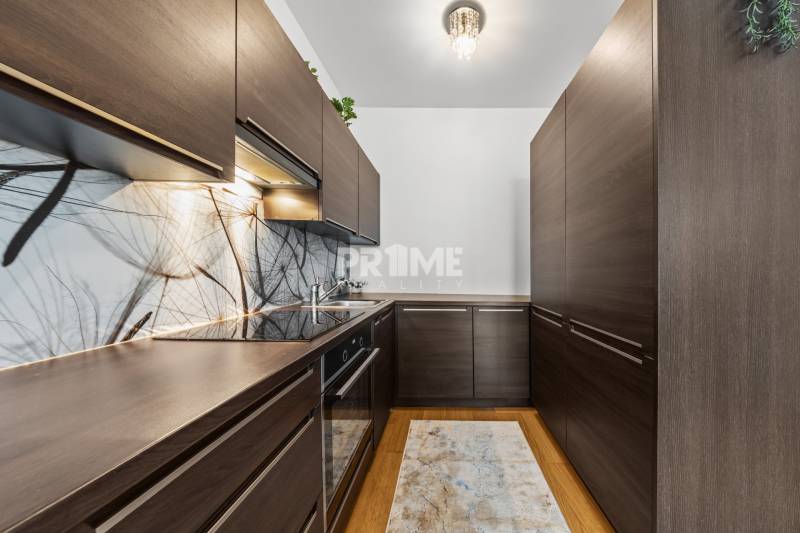 KRÁSNY 2i byt, KLÍMA, LOGGIA,VÝHĽAD,PANORAMA CITY, Landererova ulica - Kuchyňa v 2-izbovom byte s tmavým nábytkom a podlahou s dreveným dekorom.