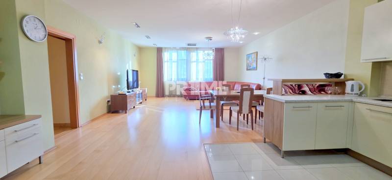 VEĽKOMETRÁŽNY 3i byt, 3 x NEPRIECHODNÁ IZBA, KLÍMA, BALKÓN, Nám.SNP - Obývacia izba v 3-izbovom byte s podlahou s dreveným dekorom, súčasťou je kuchyňa a jedálenský stôl.